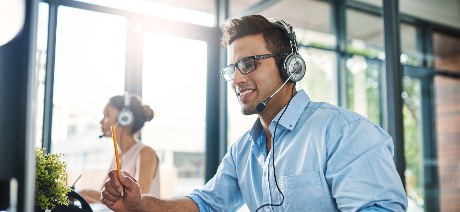 © iStock-1132874986_PeopleImages (Cropped shot of a handsome young man working in a call center with a female colleague in the background)